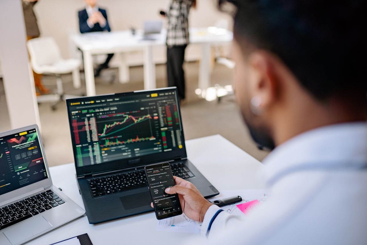 The Art of Drawing Readers In: Your attractive post title goes here A businessman using smartphone and laptop to track stock market trends in a modern office setting.