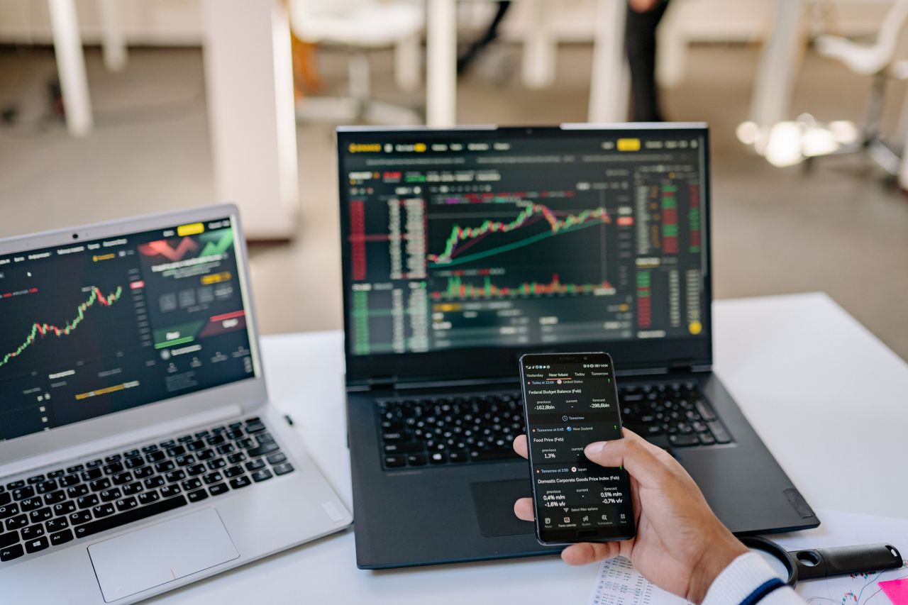 Mastering the First Impression: Your intriguing post title goes here A professional tracks stock market trends using two laptops and a smartphone, showcasing digital finance tools.